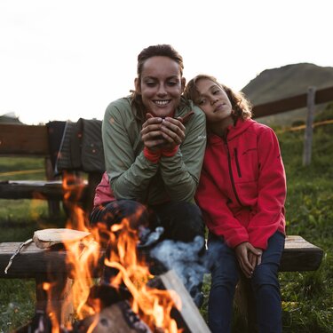 Zwei Personen genießen eine warme Tasse am Lagerfeuer im Freien.