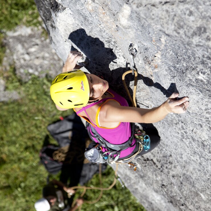 Eine Frau mit gelbem Helm klettert eine steile Felswand hinauf.