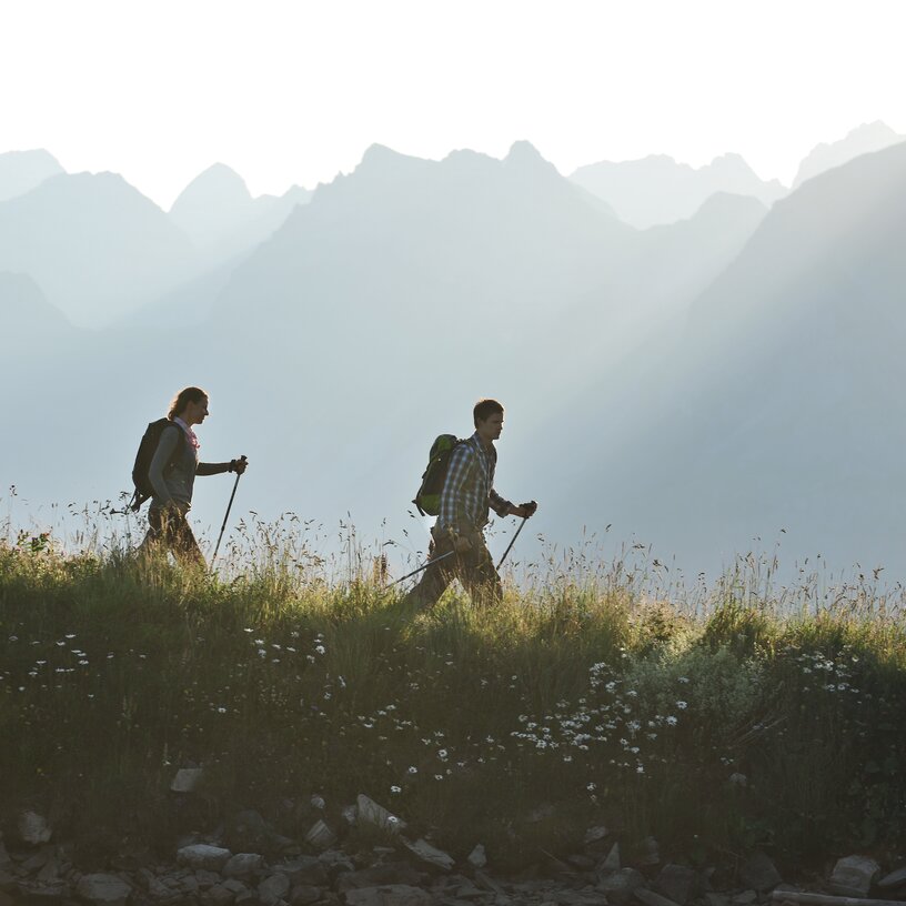 Zwei Wanderer mit Rucksäcken und Stöcken auf einem Bergpfad.