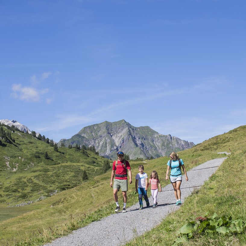 Familie wandert auf einem Pfad durch die Alpenlandschaft.