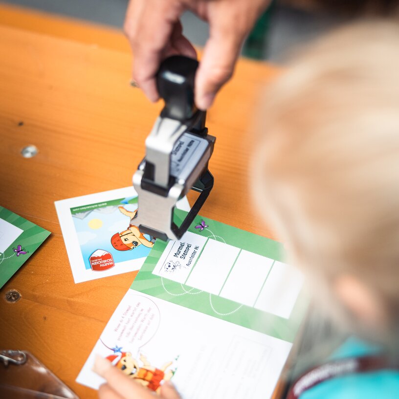 Eine Person stempelt einen Kinderpass, während ein Kind zuschaut.