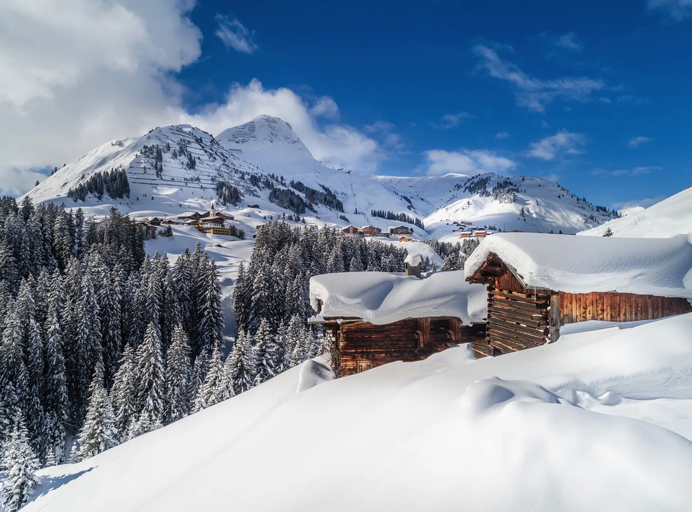 Verschneite Holzhütten in Warth-Schröcken am Arlberg mit Bergen im Hintergrund.