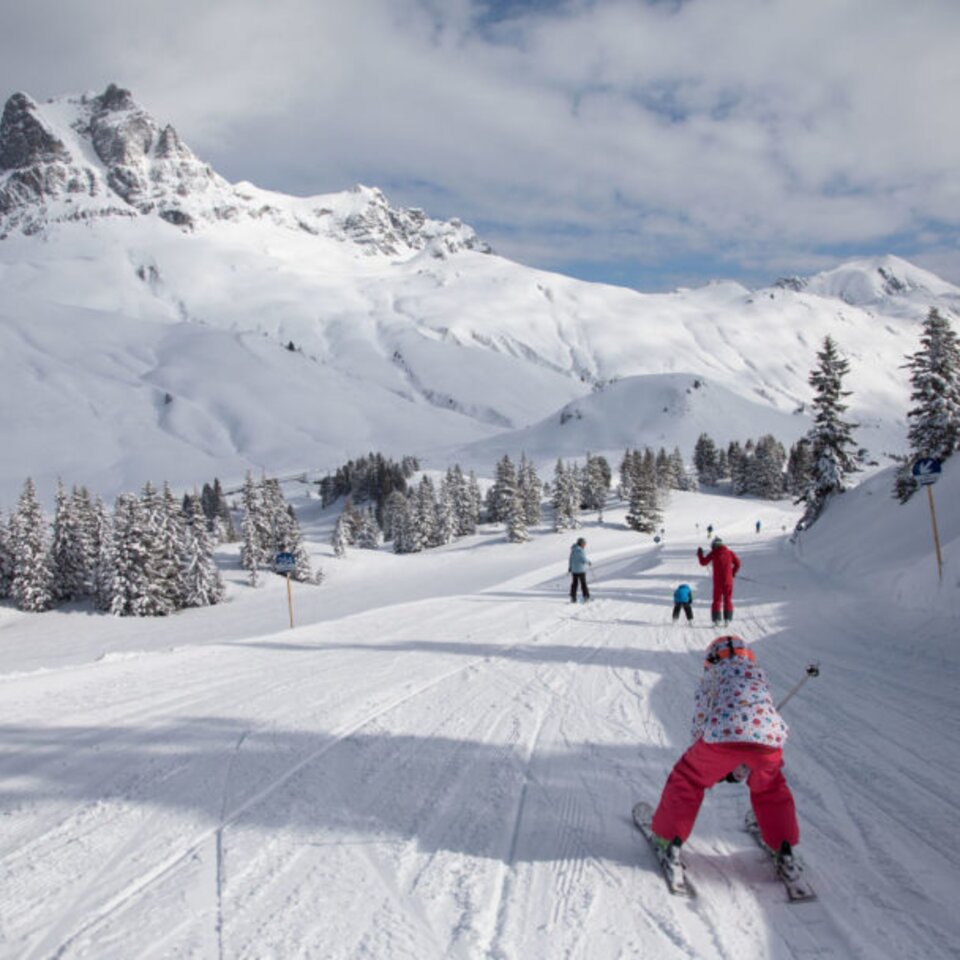 Skifahrer auf einer verschneiten Piste mit Bergpanorama.