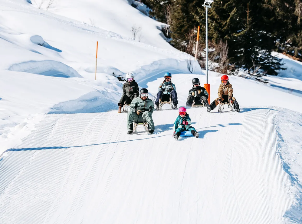 Fünf Personen rodeln eine schneebedeckte Piste hinunter.