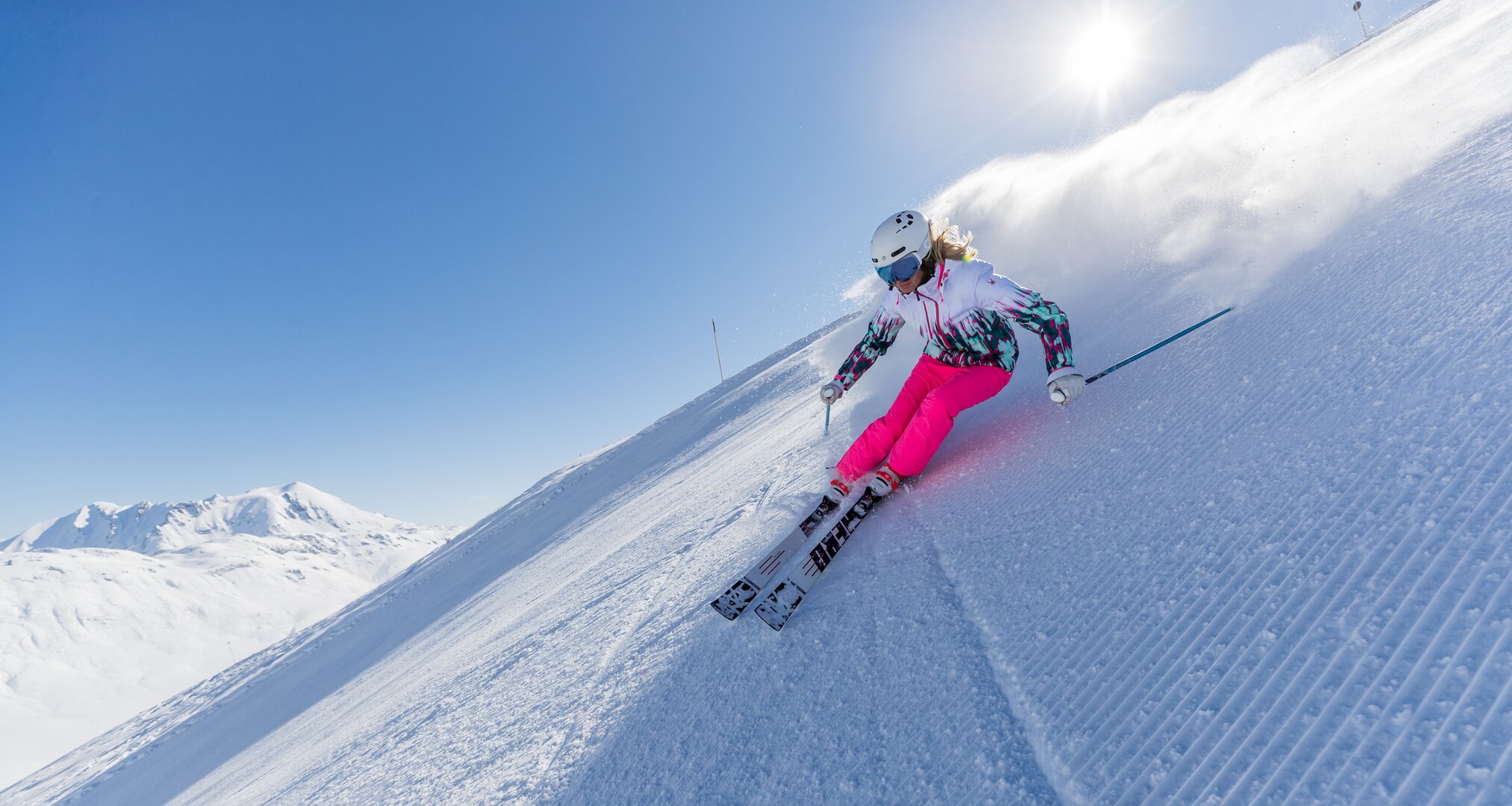Skifahrerin mit pinker Skihose bei sonnigem Wetter auf einer Piste.